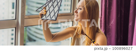 Young woman does makeup sitting by the window with a panoramic view of the skyscrapers and the big city BANNER, LONG FORMAT 100896027