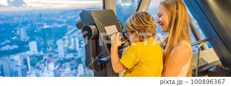 Mom and son are looking at Kuala lumpur cityscape. Use binoculars. Panoramic view of Kuala Lumpur city skyline evening at sunset skyscrapers building in Malaysia. Traveling with kids concept BANNER Mom and son are looking at Kuala lumpur cityscape. Use binoculars. Panoramic view of Kuala Lumpur city skyline evening at sunset skyscrapers building in Malaysia. Traveling with kids concept BANNER 100896367