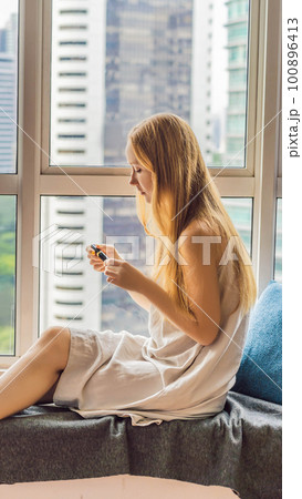 Young woman does makeup sitting by the window with a panoramic view of the skyscrapers and the big city VERTICAL FORMAT for Instagram mobile story or stories size. Mobile wallpaper Young woman does makeup sitting by the window with a panoramic view of the skyscrapers and the big city VERTICAL FORMAT for Instagram mobile story or stories size. Mobile wallpaper 100896413