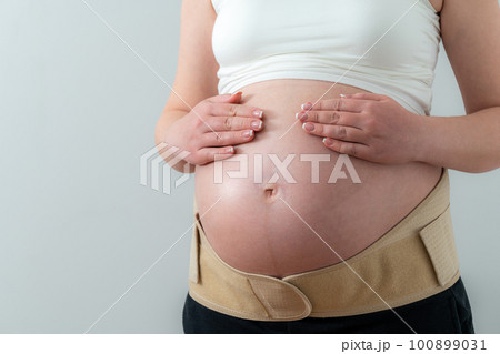 Belly of pregnant woman in bandage. Orthopedic abdominal support belt 100899031