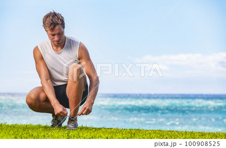 Exercise fitness man getting ready to run walk tying running shoes healthy active outdoor lifestyle walking at beach 100908525