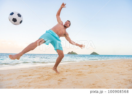 Beach soccer man playing barefoot on sand for recreational fun. Happy athlete kicking ball in the air Beach soccer man playing barefoot on sand for recreational fun. Happy athlete kicking ball in the air 100908568