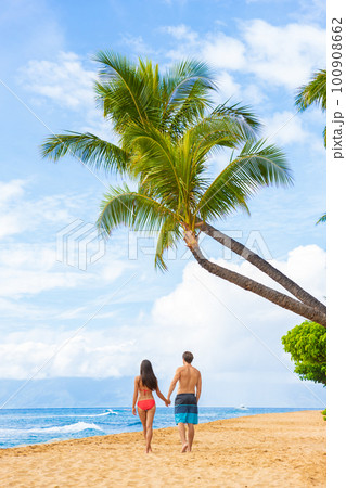Hawaii beach couple walking on Kaanapali Maui Hawai travel. Two adults tourist on sunset stroll romantic vacation travel holiday. Vertical shot with palm trees tropical background Hawaii beach couple walking on Kaanapali Maui Hawai travel. Two adults tourist on sunset stroll romantic vacation travel holiday. Vertical shot with palm trees tropical background 100908662