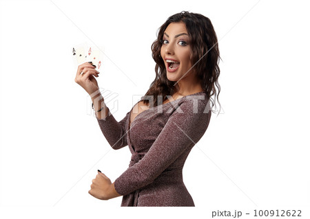 Brunette girl wearing shiny brown dress posing with two playing cards in her hand standing isolated on white background. Casino, poker. Close-up. 100912622