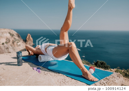 Woman sea pilates. Sporty happy middle aged woman practicing fitness on yoga mat with balls and roller near sea, smiling active female outside, enjoying healthy lifestyle, harmony and meditation. 100914124