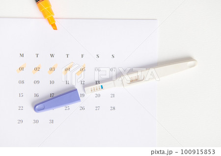 Top view of inkjet pregnancy test with a biochemical reaction between hCG and urine appearing in two bars above a white calendar with last menstrual dates marked. Rapid diagnosis of pregnancy at home 100915853