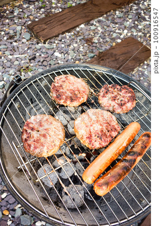 バーベキューコンロで焼かれているハンバーグとフランクフルト 100916547