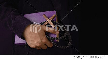 Spirituality, Religion and Hope Concept. Person Holding a Holy Bible, Bead and Cross. Symbol of Humility, Supplication, Believe and Faith for Christian People. Dark Tone, Close-Up and Side View 100917297