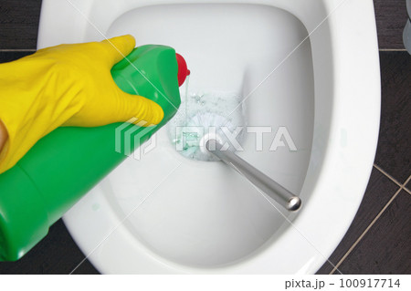 Person in yellow rubber gloves cleans the toilet bowl with a brush and disinfectant Person in yellow rubber gloves cleans the toilet bowl with a brush and disinfectant 100917714