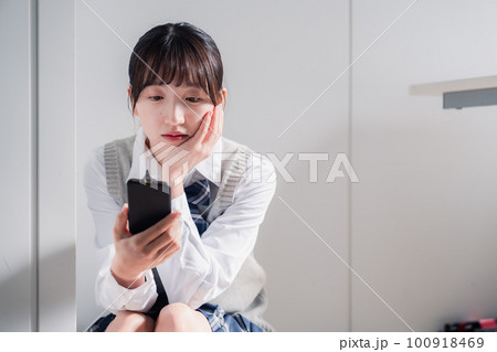 スマホを見ながら落ち込む女子高生 スマホを見ながら落ち込む女子高生 100918469