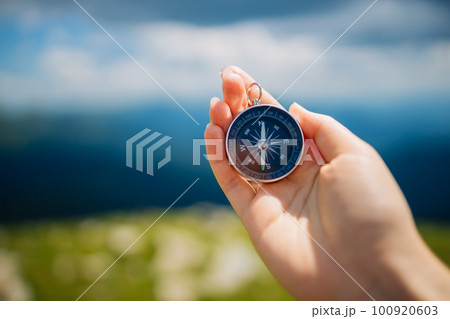Traveler woman hand holds a hand-held compass against the backdrop of mountains and hills at sunset. The concept of travel and navigation in open areas 100920603