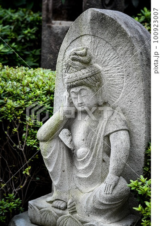 街角に立膝に肘をついている小さな仏像が設置されている風景 100923007