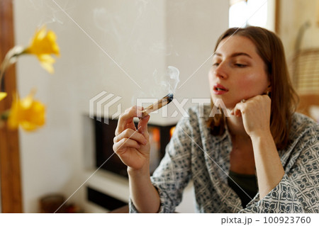 Woman hands burning Palo Santo, before ritual on the table with candles and green plants. Smoke of smudging treats pain and stress, clears negative energy and meditation wooden stick Woman hands burning Palo Santo, before ritual on the table with candles and green plants. Smoke of smudging treats pain and stress, clears negative energy and meditation wooden stick 100923760