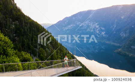 Young man standing on the viewing platform with drone controller view of Hallstatt lake, mountains 100924036