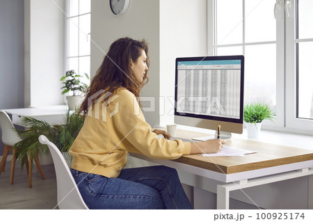 Young woman accountant working at her home office and using spreadsheets on the computer 100925174