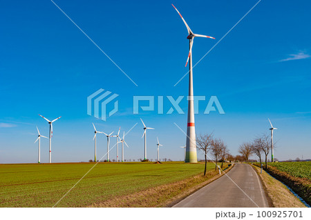 View over beautiful farm landscape with early spring agriculture field, wind turbines to produce green energy and a lonely road near Mittweida, Germany, at blue sunny sky. 100925701