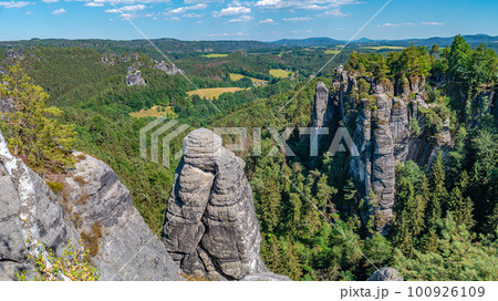 Panoramic over monumental Bastei sandstone pillars, rock formation and stacks surrounded by ancient forests at Kurort Rathen village in the national park Saxon Switzerland by Dresden, Saxony, Germany. Panoramic over monumental Bastei sandstone pillars, rock formation and stacks surrounded by ancient forests at Kurort Rathen village in the national park Saxon Switzerland by Dresden, Saxony, Germany. 100926109