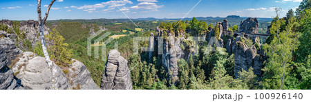 Panoramic over monumental Bastei sandstone pillars, rock formation and stacks surrounded by ancient forests at Kurort Rathen village in the national park Saxon Switzerland by Dresden, Saxony, Germany. Panoramic over monumental Bastei sandstone pillars, rock formation and stacks surrounded by ancient forests at Kurort Rathen village in the national park Saxon Switzerland by Dresden, Saxony, Germany. 100926140