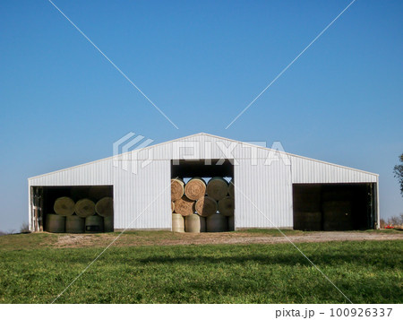Granular old photo of round hay bales stacked in a sheet metal tin barn on a rural farm. 100926337