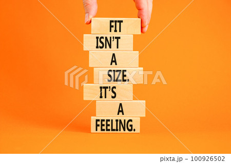 Fit, size or feeling symbol. Concept words Fit is not a size it is a feeling on wooden blocks. Beautiful orange background. Copy space. Businessman hand. Motivational fit size or feeling concept. 100926502