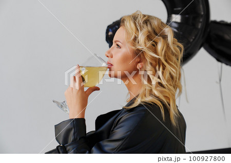 an attractive blonde in a black leather coat with a glass of champagne. an attractive blonde in a black leather coat with a glass of champagne. 100927800