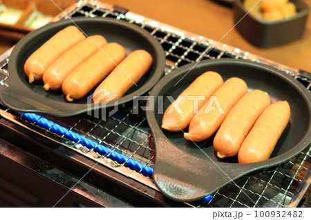 卓上コンロ上の丸型フライパンで焼かれるウインナーソーセージ 100932482