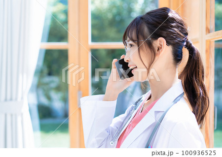 窓際でスマホで電話する若い女性医師 100936525