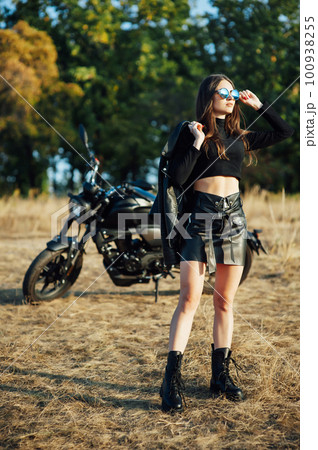 beautiful girl biker in black clothes stands at the motorcycle with a safety helmet in his hands 100938255