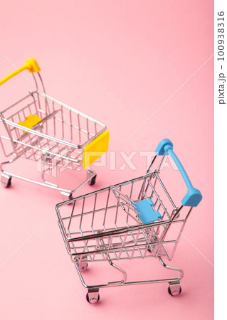 Mini shopping trolleys on pink background. Vertical photo Mini shopping trolleys on pink background. Vertical photo 100938316