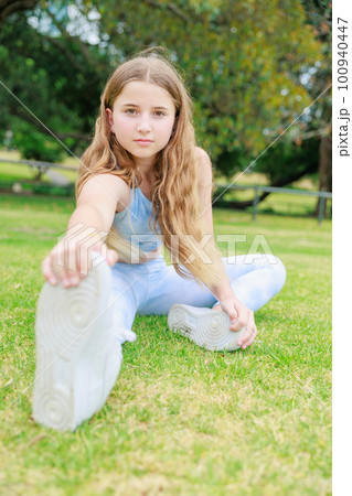 公園の芝生に座りストレッチをするオーストラリアの中学生（縦写真） 100940447