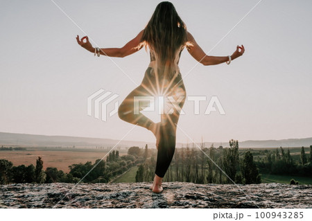 Fitness woman. Well looking middle aged woman with long hair, fitness instructor in leggings and tops doing stretching and pilates on the rock near forest. Female fitness yoga routine concept. 100943285
