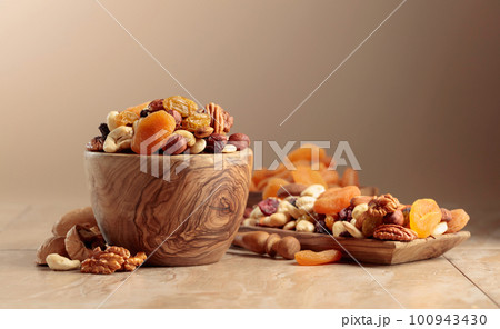 Dried fruits and nuts on a beige ceramic table. 100943430