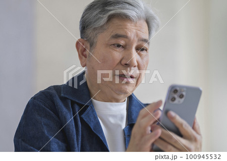 スマートフォンの画面を見るシニア男性 100945532