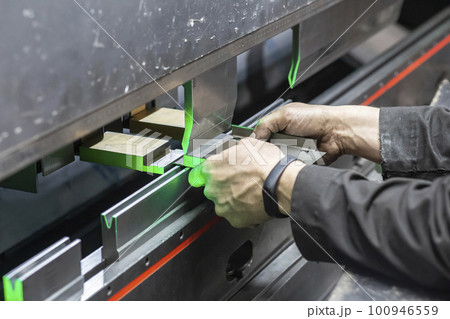 Worker holds a part in a CNC bending machine Worker holds a part in a CNC bending machine 100946559