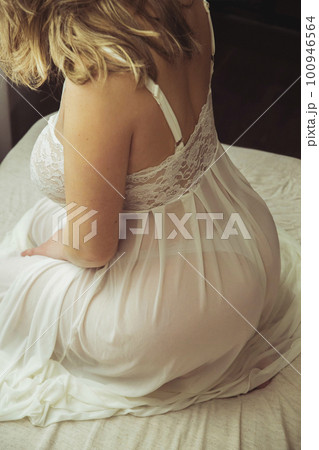 Beautiful blonde with big breasts sitting on the bed in a nightie 100946564