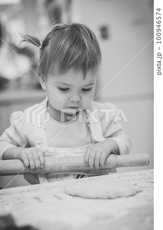 Adorable baby in an apron is rolling out the dough in the kitchen Adorable baby in an apron is rolling out the dough in the kitchen 100946574