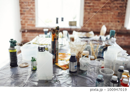 Buckets with paint, dirty glass jars, brushes, spray gun, solvents and other art supplies Buckets with paint, dirty glass jars, brushes, spray gun, solvents and other art supplies 100947019