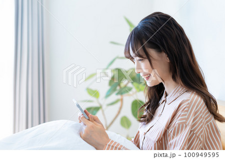 ベッドでスマホ動画を観るパジャマの若い女性 100949595