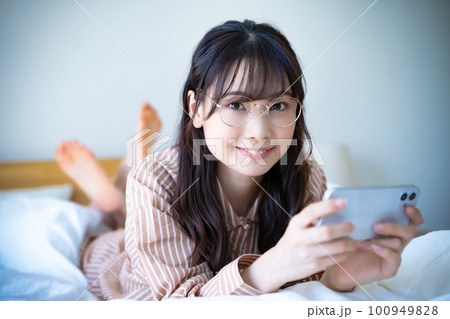 ベッドでスマホ動画を観るパジャマの若い女性 ベッドでスマホ動画を観るパジャマの若い女性 100949828