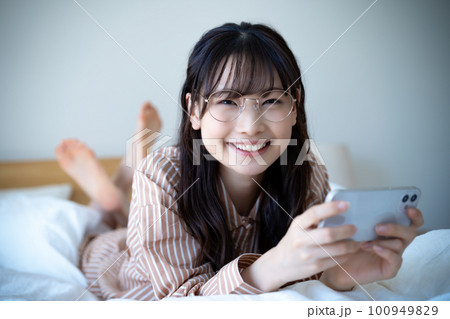 ベッドでスマホ動画を観るパジャマの若い女性 ベッドでスマホ動画を観るパジャマの若い女性 100949829