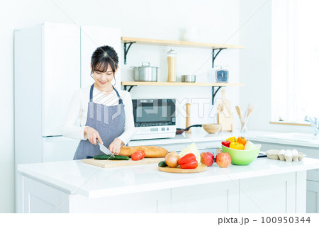 キッチンで料理をするエプロンの若い女性 100950344