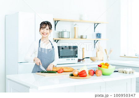 キッチンで料理をするエプロンの若い女性 100950347