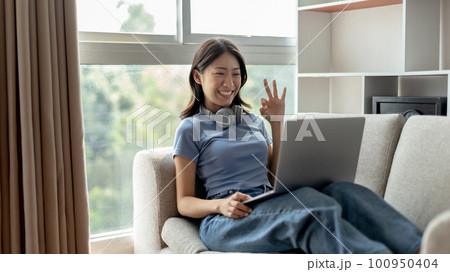 Young Asian woman greets his friends and teachers in a live video with a smile on his face, Online communication , Stay home, New normal, VDO Call, Social distancing, Internet learning. Young Asian woman greets his friends and teachers in a live video with a smile on his face, Online communication , Stay home, New normal, VDO Call, Social distancing, Internet learning. 100950404