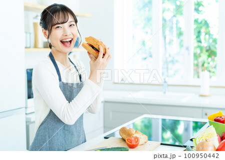 キッチンで料理をするエプロンの若い女性 100950442