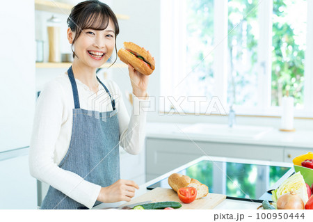 キッチンで料理をするエプロンの若い女性 100950444