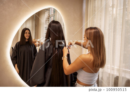 Pretty brunette young woman looks into a huge mirror when her luxurious long hair is cut off Pretty brunette young woman looks into a huge mirror when her luxurious long hair is cut off 100950515