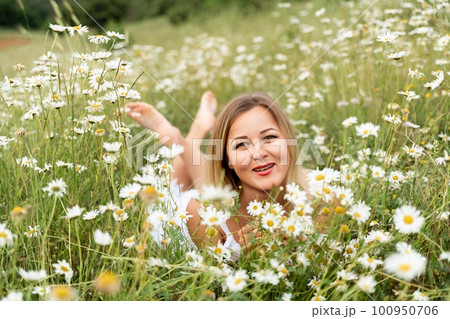 A woman lies in a chamomile field, dressed in a white dress 100950706