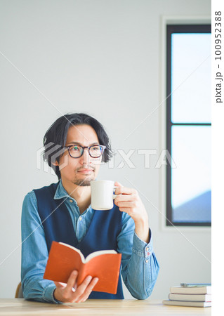 自宅の書斎でコーヒーを飲みながら本を読む若い男性 自宅の書斎でコーヒーを飲みながら本を読む若い男性 100952388