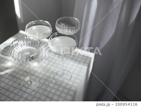 Champagne glasses on a light table surface reflecting soft sunshine rayson Champagne glasses on a light table surface reflecting soft sunshine rayson 100954116