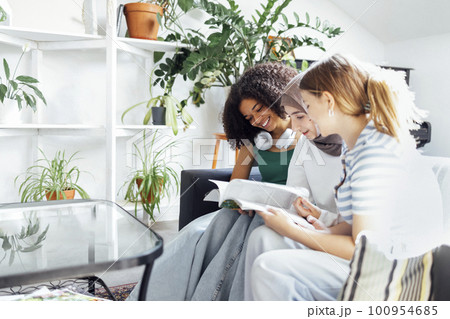 Three pretty female teenagers of different nationalities are reading a magazine and smiling 100954685
